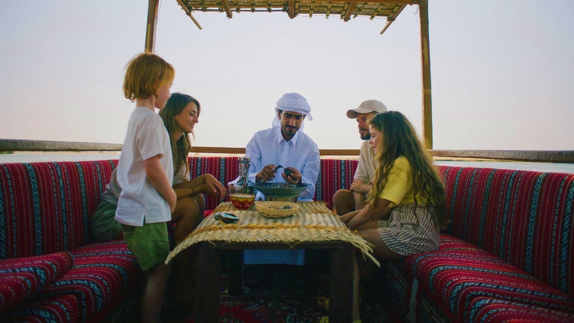 Family gathering on traditional red patterned seating in a Bedouin tent with host serving refreshments and dates